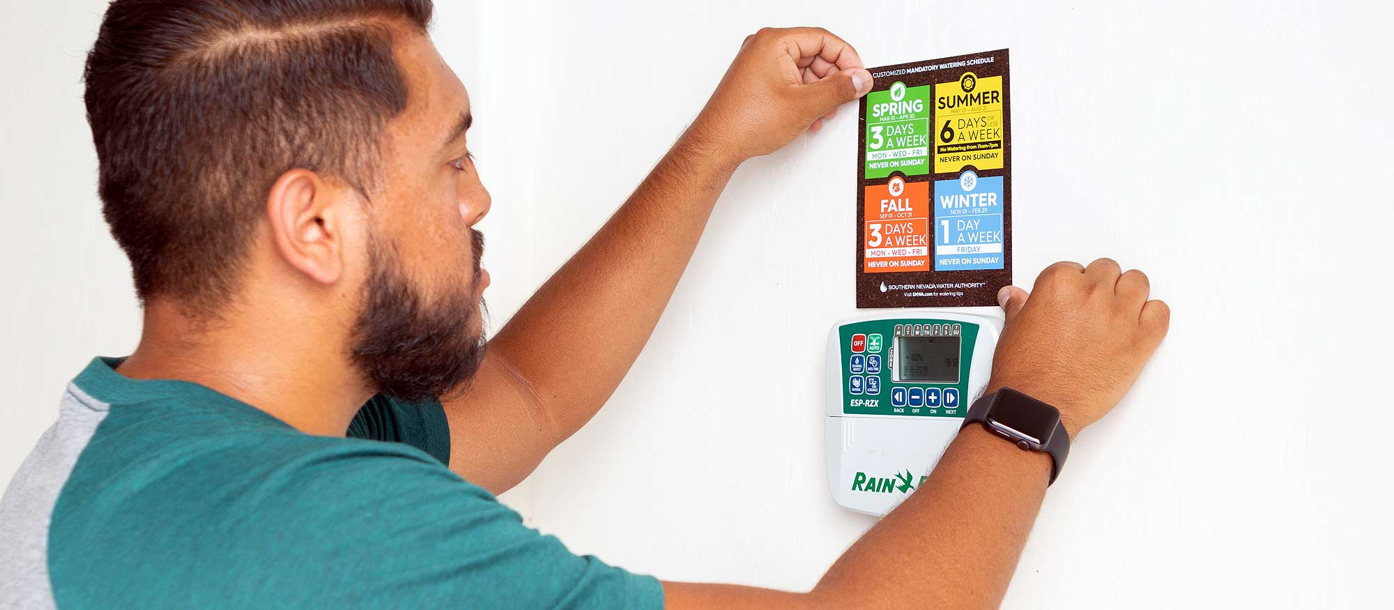 Person hangs watering schedule next to watering clock in garage