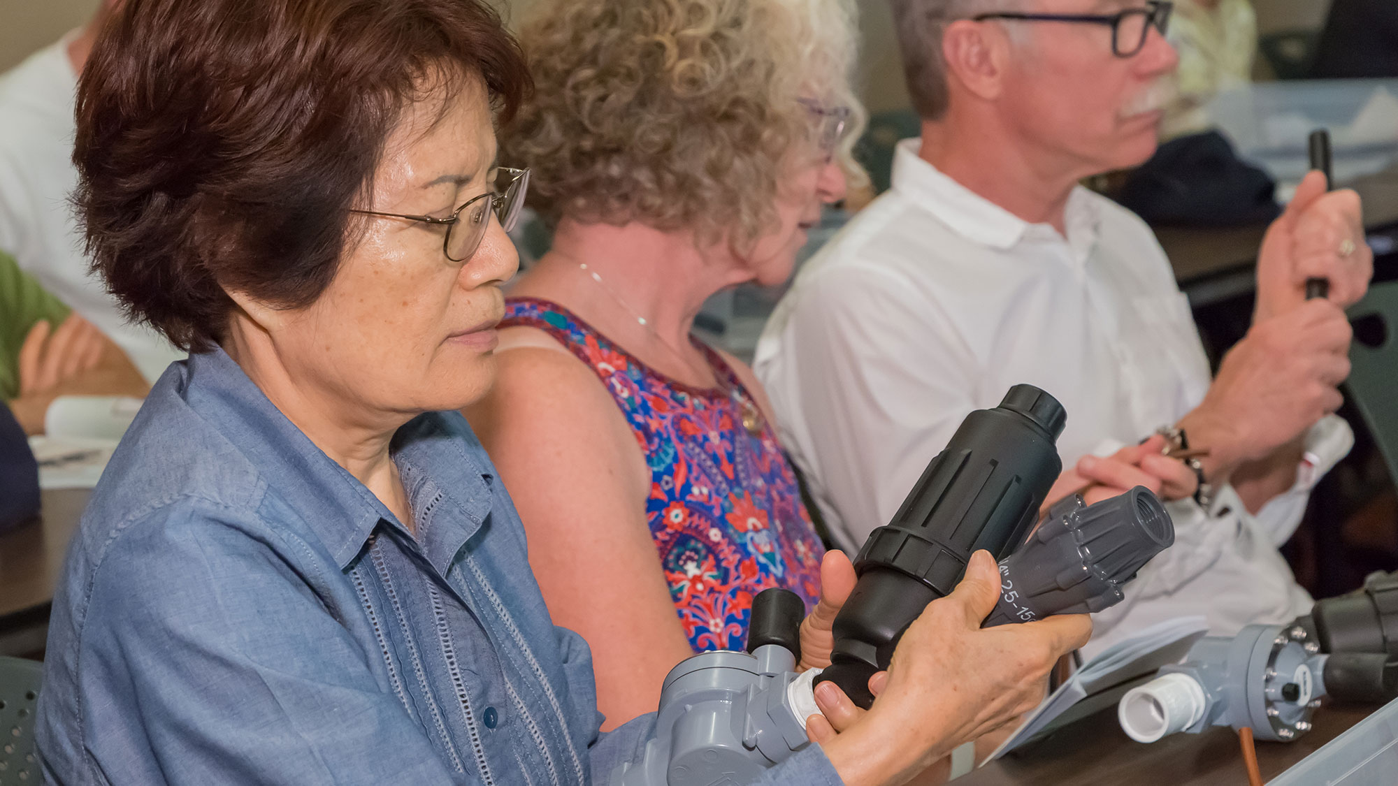 Two women and a man learn how to put together components of a drip irrigation system in a class.