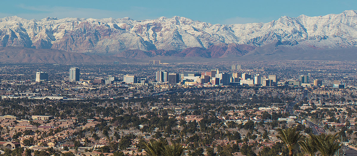 <img alAn aerial view of Las Vegas with snow-covered mountains in the background