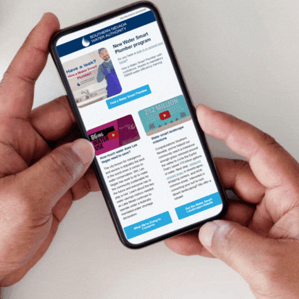 Hand holding a mobile phone displaying the SNWA enewsletter and popup text reminder about seasonal watering restrictions