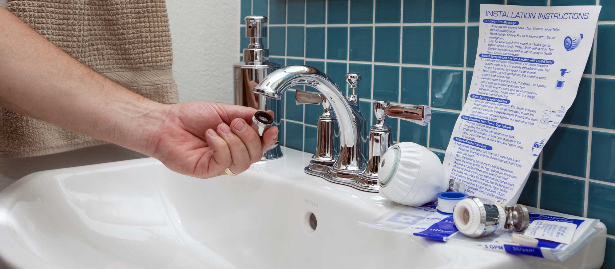 Close up of hand holding aerator with bathroom sink and Water Audit Kit in background