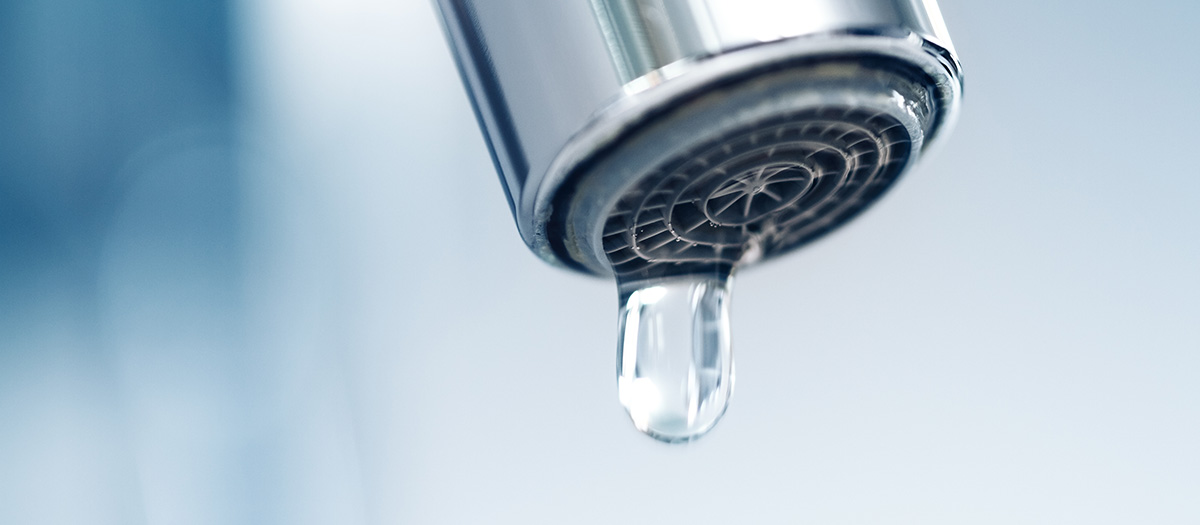 A drop of water hanging from an indoor faucet.