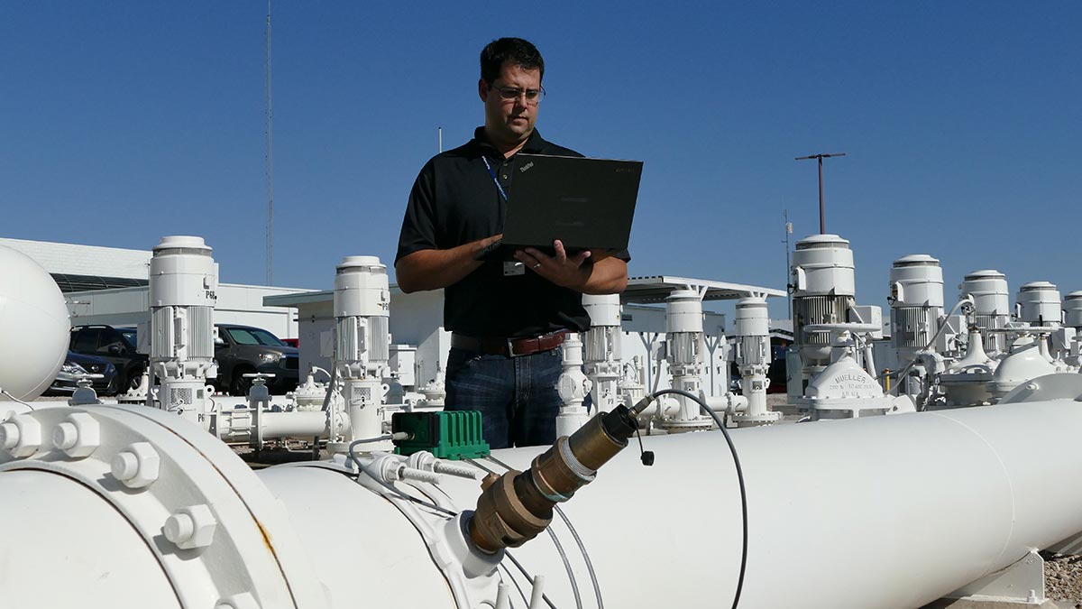 Technician using a laptop on a large water pipe.